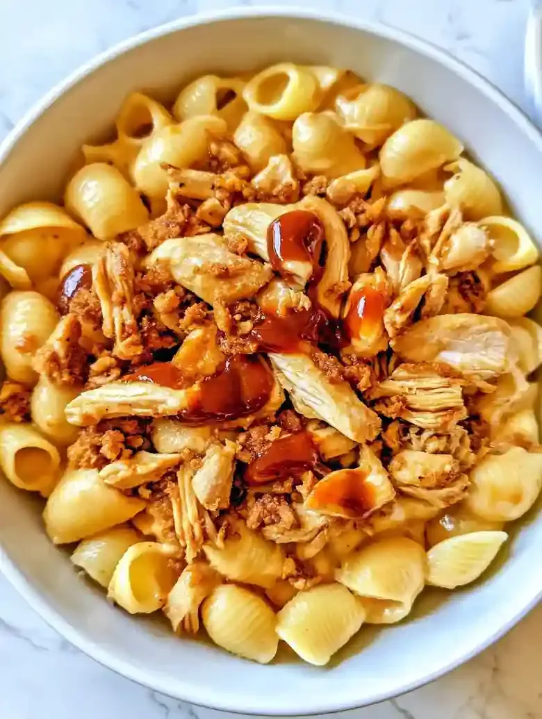 Bowl of shell pasta with cheese sauce, pulled chicken, and barbecue drizzle.