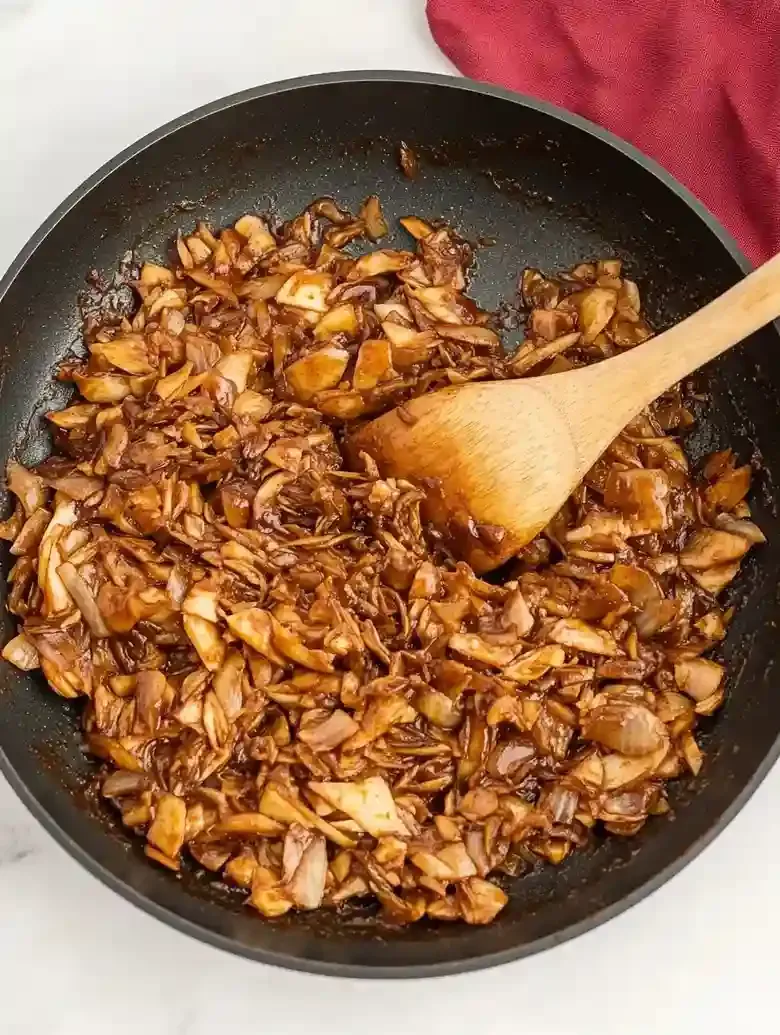 Skillet of tender, dark brown shredded vegetables being stirred with a spoon.