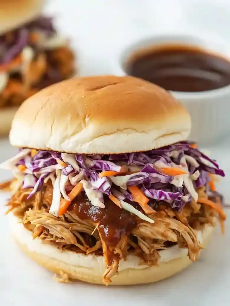 Barbecue chicken sandwich with colorful slaw on a marble surface.