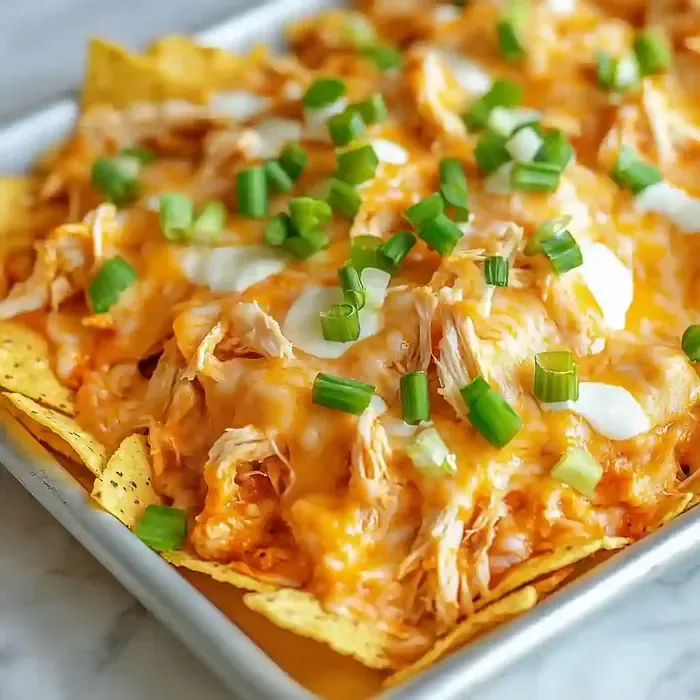 Nachos with shredded chicken, melted cheese, and green onions on marble.