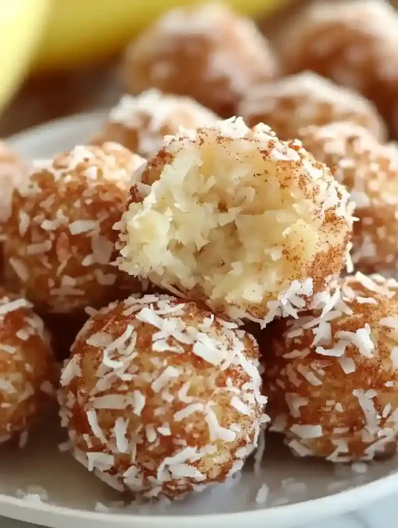 Coconut balls coated in cinnamon and shredded coconut on marble surface.