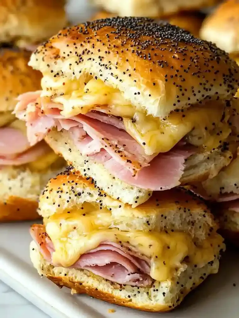 Golden-brown sliders with ham and cheese, topped with poppy seeds.