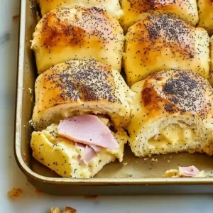 Golden-brown ham and cheese sliders on a marble surface, one slider pulled out.