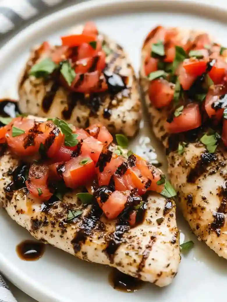 Grilled chicken pieces topped with tomato, herbs, and balsamic on marble
