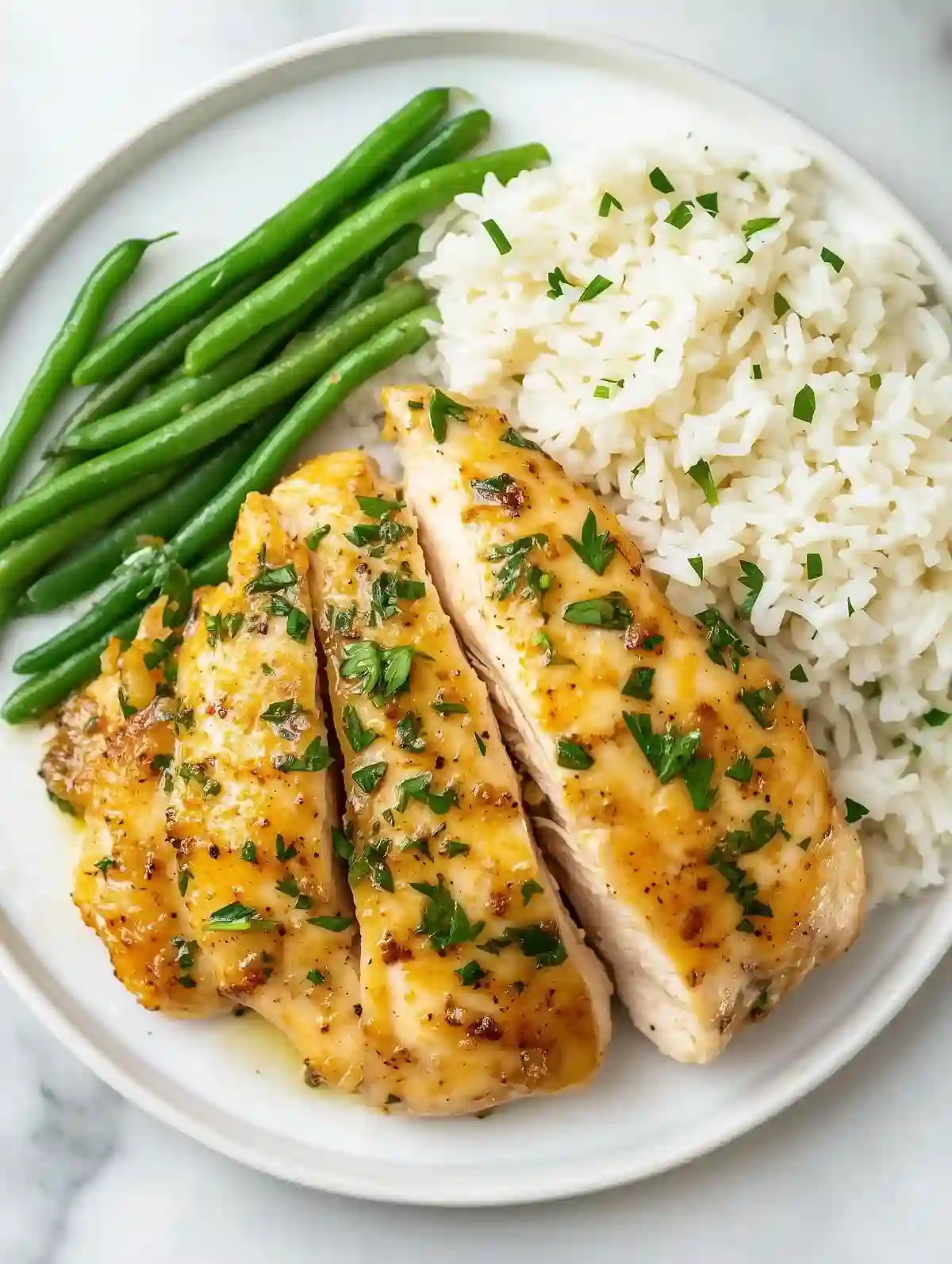 Pan-fried lemon chicken with parsley, rice, and green beans on marble surface