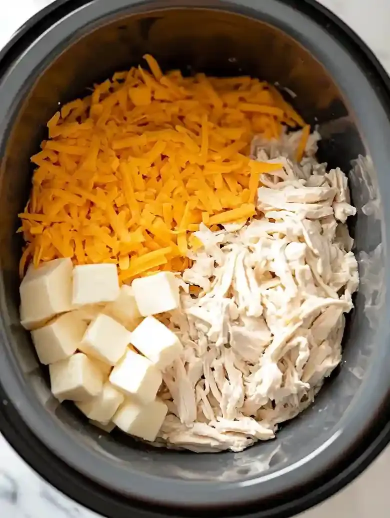 Slow cooker with shredded chicken, cream cheese, ranch, and cheddar cheese.